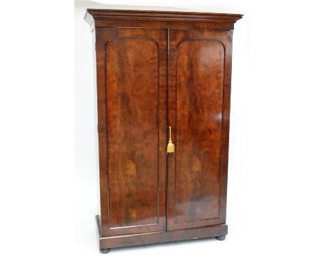 A Victorian mahogany two door wardrobe with arched panel doors, plinth base and interior drawer beneath hanging space, width 