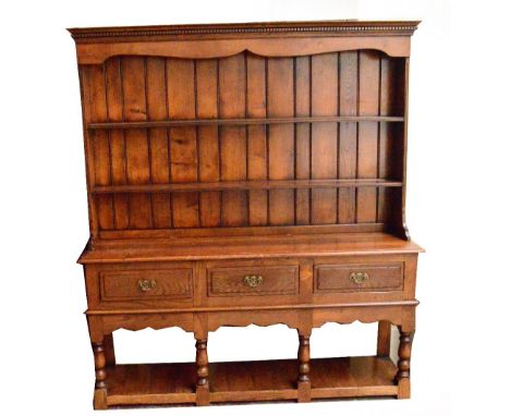 A reproduction oak dresser with boarded two-shelf plate rack above three drawers and apron, on ring turned front supports, un