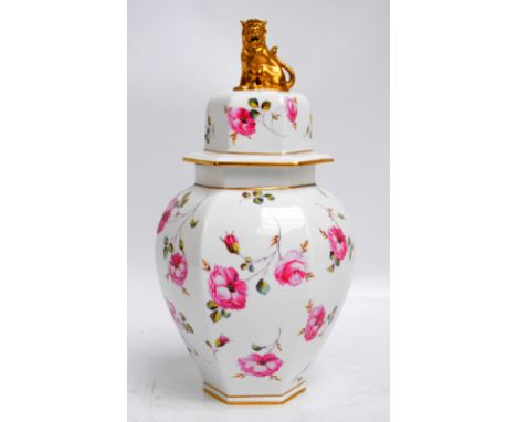 A Royal Crown Derby rose decorated hexagonal baluster vase and cover surmounted with a seated lion and with red printed marks