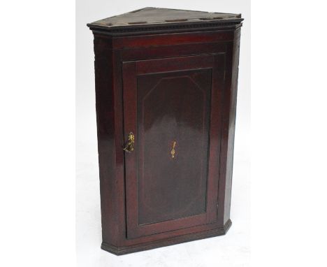 A Georgian mahogany flat fronted wall hanging corner cupboard, the single door centred with floral inlaid panel enclosing fou