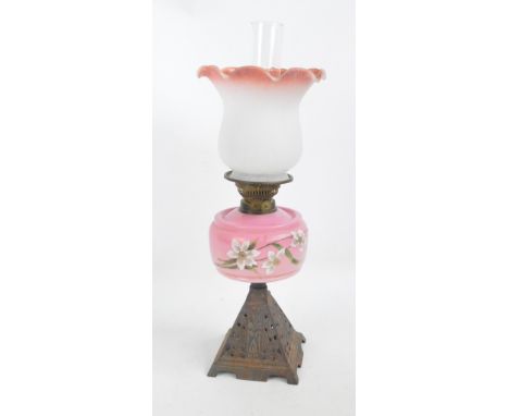 A Victorian cast iron oil lamp with pink glass floral hand painted reservoir and opaque white and pink tulip shaped shade, he