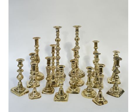 A group of brass candlestick holders comprising a large pair with faceted stem (h- 38cm), and a mixed group including circula