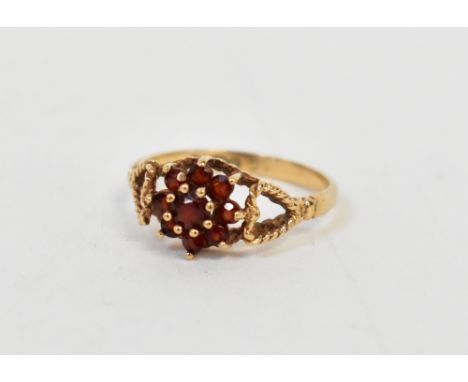 A 9ct gold garnet cluster ring with central claw set garnet within a border of eight smaller claw set stones, with open love 