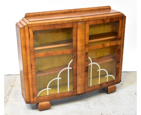 An Art Deco style walnut display cabinet with architectural moulded top, the angled front centred with slim bowed panel flank