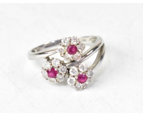 A modern contemporary 14ct white gold diamond and ruby ring, the three crossover arms each with a flowerhead with a central c