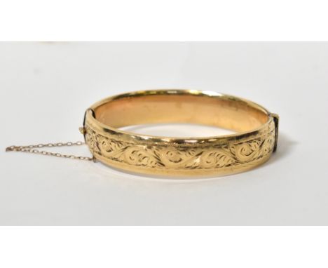 A 9ct yellow gold hinged bangle, with incised floral decoration to one side and a fine link safety chain, dimensions when clo