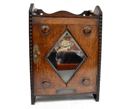 An early 20th century oak smoker's cabinet with a bevel edged lozenge glass to the door and two drawers to the interior, with