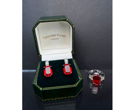 A white metal ring stamped '925' set with oval ruby colour stone (tests possibly synthetic) and clear stones to either side w