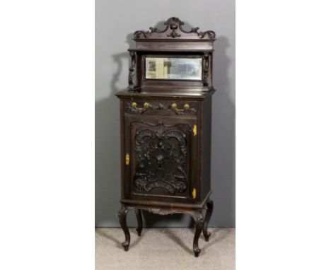 A late Victorian mahogany music cabinet carved in relief throughout with leaf scroll ornament, the upper part with one open s