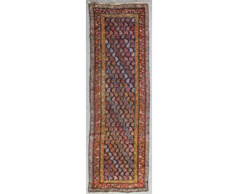 An antique Caucasian runner woven in colours with endless boteh repeats on a dark blue ground within stylized floral three st