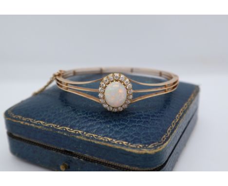 An opal and diamond hinged bangle, with an oval opal, approximately 11mm x 9mm surrounded by round old cut diamonds, each app