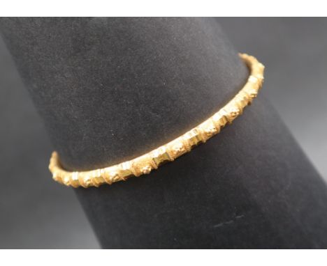 A yellow metal bangle decorated with flower heads, 75mm diameter, approximately 15 grams