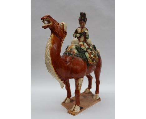 A Tang Dynasty style pottery statuette of a braying camel mounted with a female court musician playing a pipe, in brown, crea
