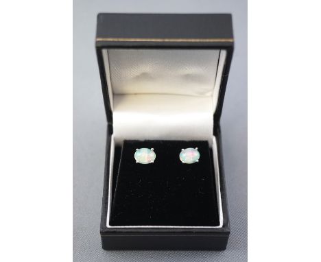 A white metal pair of single stone stud earrings. Each set with a cabochon cut Ethiopian welo opal. Post and scroll fittings.