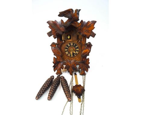 A SWiss carved wood musical cuckoo clock carved with leaves, two woodpeckers and a bird, with two doors opening to reveal a b