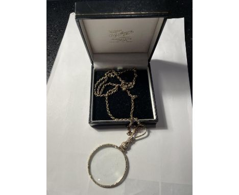 A YELLOW METAL CHAIN WITH A DECORATIVE MAGNIFYING GLASS PENDANT IN A PRESENTATION BOX 