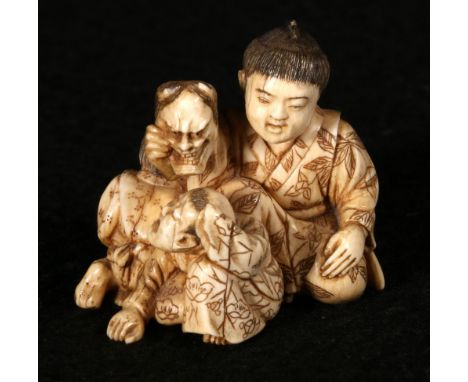 Japanese netsuke depicting a boy holding up a mask with two other children beside him, signed, 4cm, Meiji CONDITION REPORT: H
