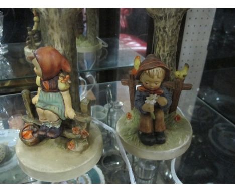 A PAIR OF HUMMEL TABLE LAMPS each modelled as a tree stump with figures seated on a fence together with porcelain figure flow