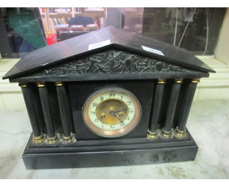 A BLACK SLATE MANTLE CLOCK of architectural form the frieze embossed with warriors above a circular dial flanked on each side