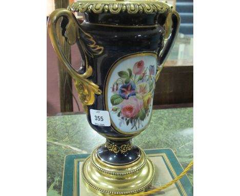 A PORCELAIN AND BRASS TABLE LAMP of urn form the blue and gilt ground with floral painted panel raised on a circular stepped 