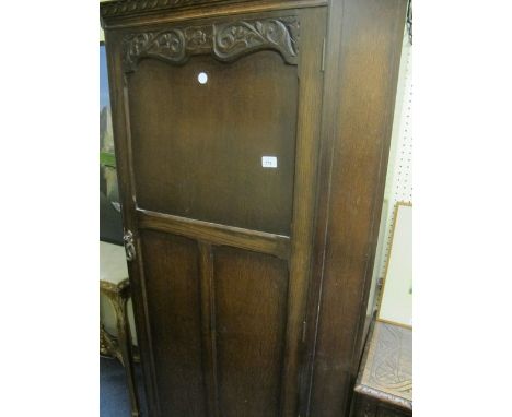 AN OAK WARDROBE the moulded cornice above a carved and moulded door between canted angles interior with hanging rail and shel