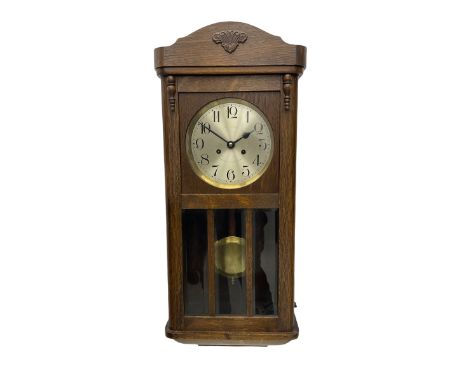 A 1930's wall clock in an oak case with a full-length door, three glazed panels and visible pendulum, case with a shaped pedi