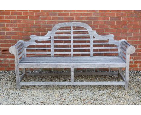 A Lutyens-style teak garden bench with scrolling arms and camel back, 196cm wide, 62cm deep, 103.5cm highIn weathered conditi