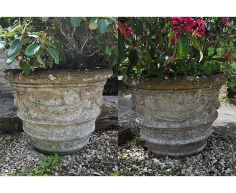 A pair of cast reconstituted stone garden urns, relief decorated with ribbon tied swags, 77cm wide, 60cm high (2)Weathered.