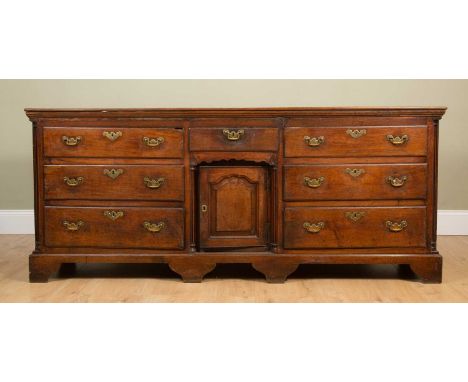A George III oak dresser base with three lines of short drawers flanking a central cupboard, with brass handles and escutcheo