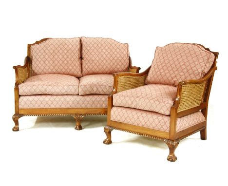 An early 20th century Bergere sofa and armchair, the mahogany frames with shaped top rails, over sweeping arms over a reeded 