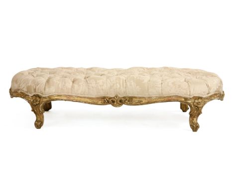 A large low giltwood stool, mid-19th century, of waisted form and with button upholstered seat, on floral carved scrolling le