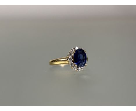 A sapphire and diamond cluster ring, the oval-cut sapphire claw-set within a band of twelve round brilliant-cut diamonds on a