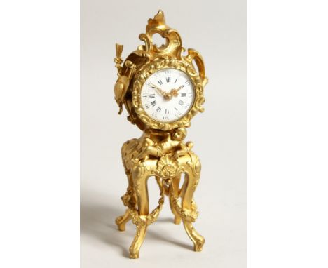  A 19TH CENTURY FRENCH GILT METAL MINIATURE CLOCK with scrolls and cherubs, drum movement on four curving legs 9ins high