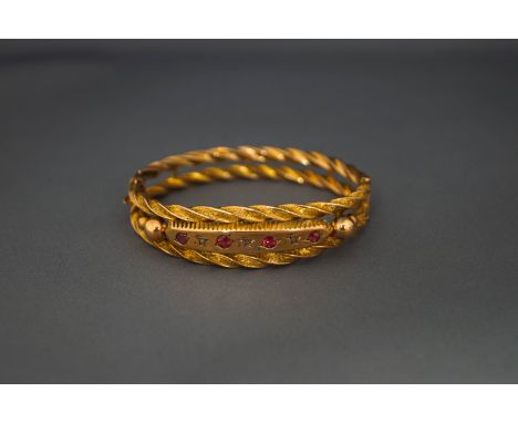 A hinged bangle, circa 1910, stamped '9ct', the frontispiece set with red pastes and rose cut diamonds, within a hollow doubl
