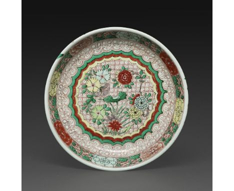 PLATen porcelaine et émaux wucai, à décor en médaillon central de pivoines, chrysanthèmes entourés de rinceaux feuillagés. (É