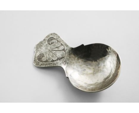 AN EARLY 20TH CENTURY HANDMADE CADDY SPOON with a hammered finish, and a lug handle, chased with a stylised shell, by Bernard