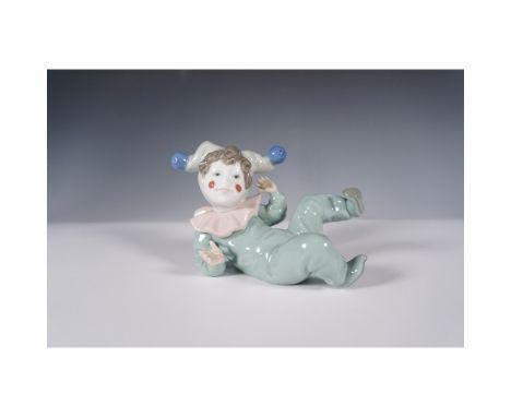 This whimsical Nao by Lladro porcelain figurine features a reclining clown in a playful pose, dressed in soft pastel tones wi