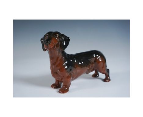 This charming Beswick figurine features a standing Dachshund rendered in a rich brown glaze with subtle shading that highligh