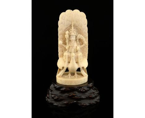 Late 19th century Japanese ivory carved as a four armed figure sitting on a lotus flower on top of a peacock, inset red carto