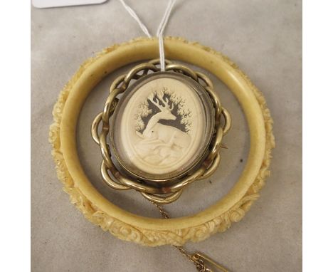 A Victorian pinchbeck swivel brooch set with an oval carved ivory plaque of a recumbent stag, against a ground of knotted fab