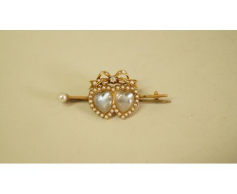 An unmarked bar brooch set two heart shaped moonstones surrounded by split pearls, with split pearl and diamond set bow above