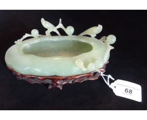 A 19th century Chinese Celadon green jade brush washer on conforming hardwood stand, naturalisticly carved in pond shape with