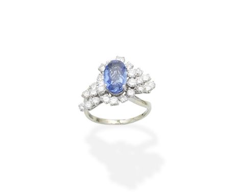 A sapphire and diamond ringThe oval-cut sapphire within a tiered cluster of obliquely-set brilliant-cut diamonds, to a crosso