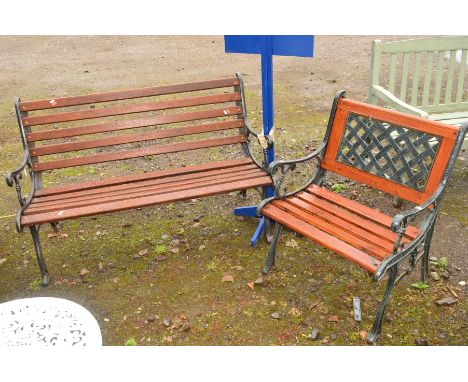 A BROWN STAINED TEAK SLATTED WOODEN BENCH with black painted cast iron ends, together with a similar garden armchair with lat