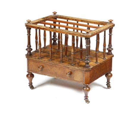 A VICTORIAN WALNUT CANTERBURY C.1860 with three divisions, supported by turned spindles, with a frieze drawer, on ceramic cas