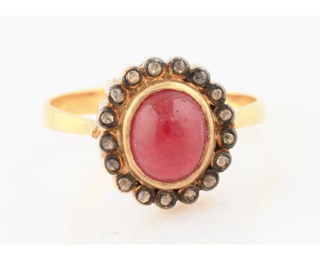 A yellow metal ruby and diamond cluster ring, the central oval ruby cabochon, measuring approx. 8x7mm, surrounded by a border