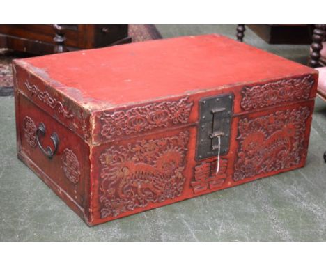 A Chinese red lacquered rectangular travelling trunk or document box, hinged cover, brass hasp, the front decorated in relief