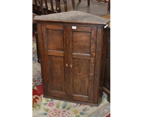 A George III elm and oak splay fronted wall hanging corner cupboard, moulded cornice above a pair of panelled doors enclosing