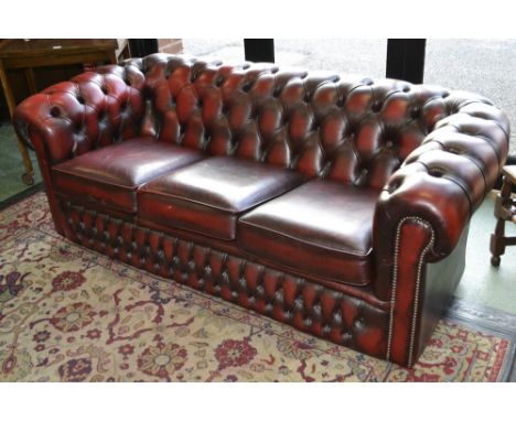 An executive office ox blood leather button upholstered three seat Chesterfield settee.