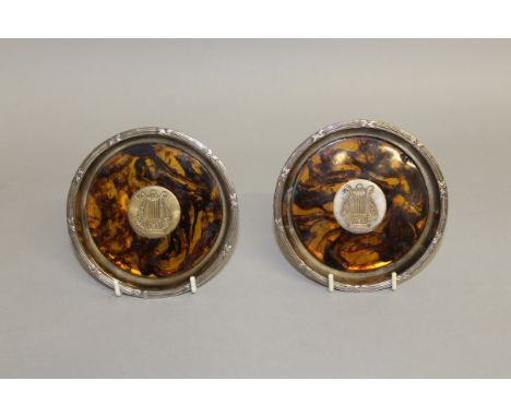 A PAIR OF FAUX TORTOISESHELL SILVER PLATE MOUNTED COASTERS with an inset plaque Harp.  4.5ins diameter. 